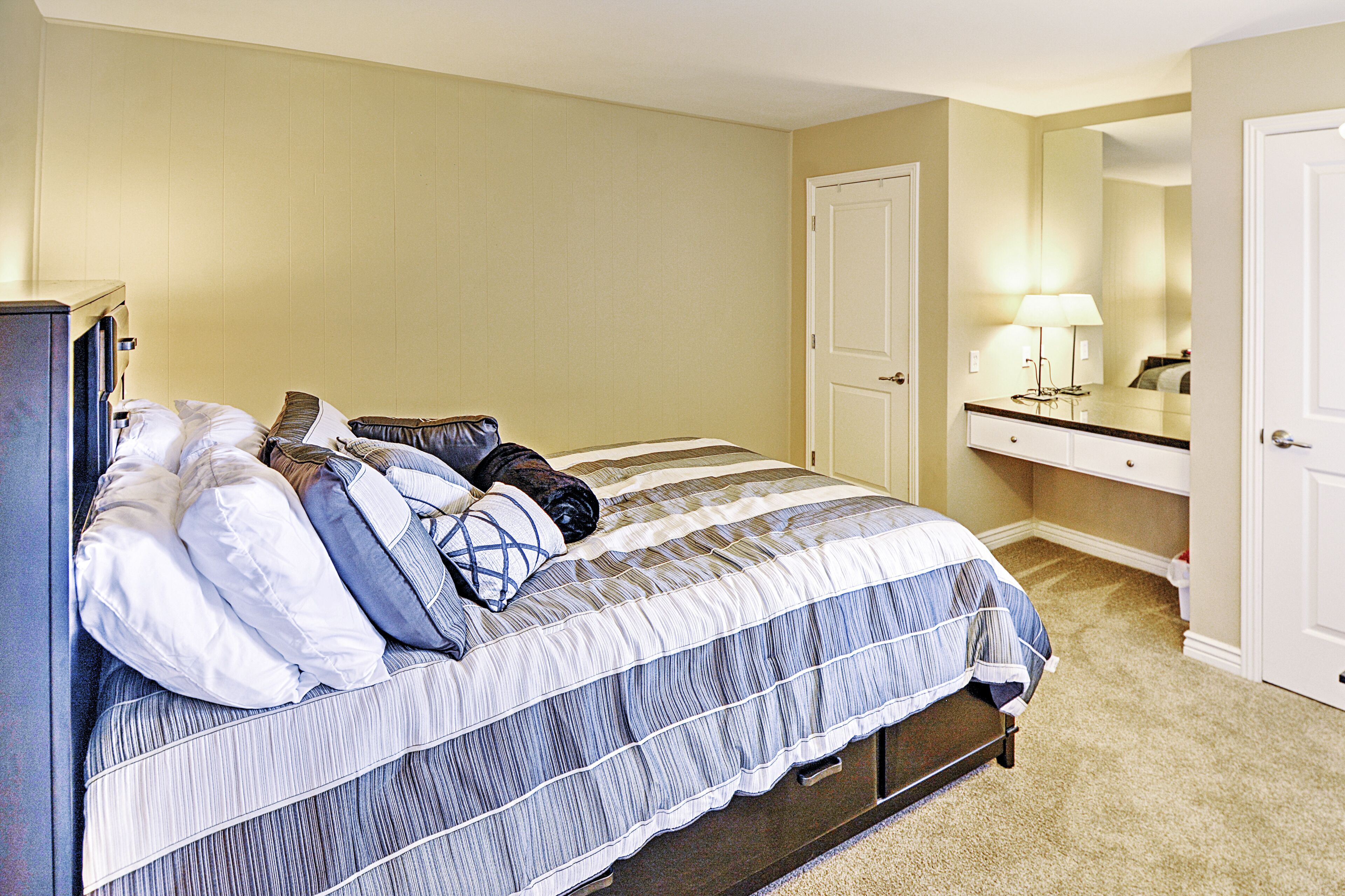 A bedroom with a bed, a dresser, a mirror, and a door.
