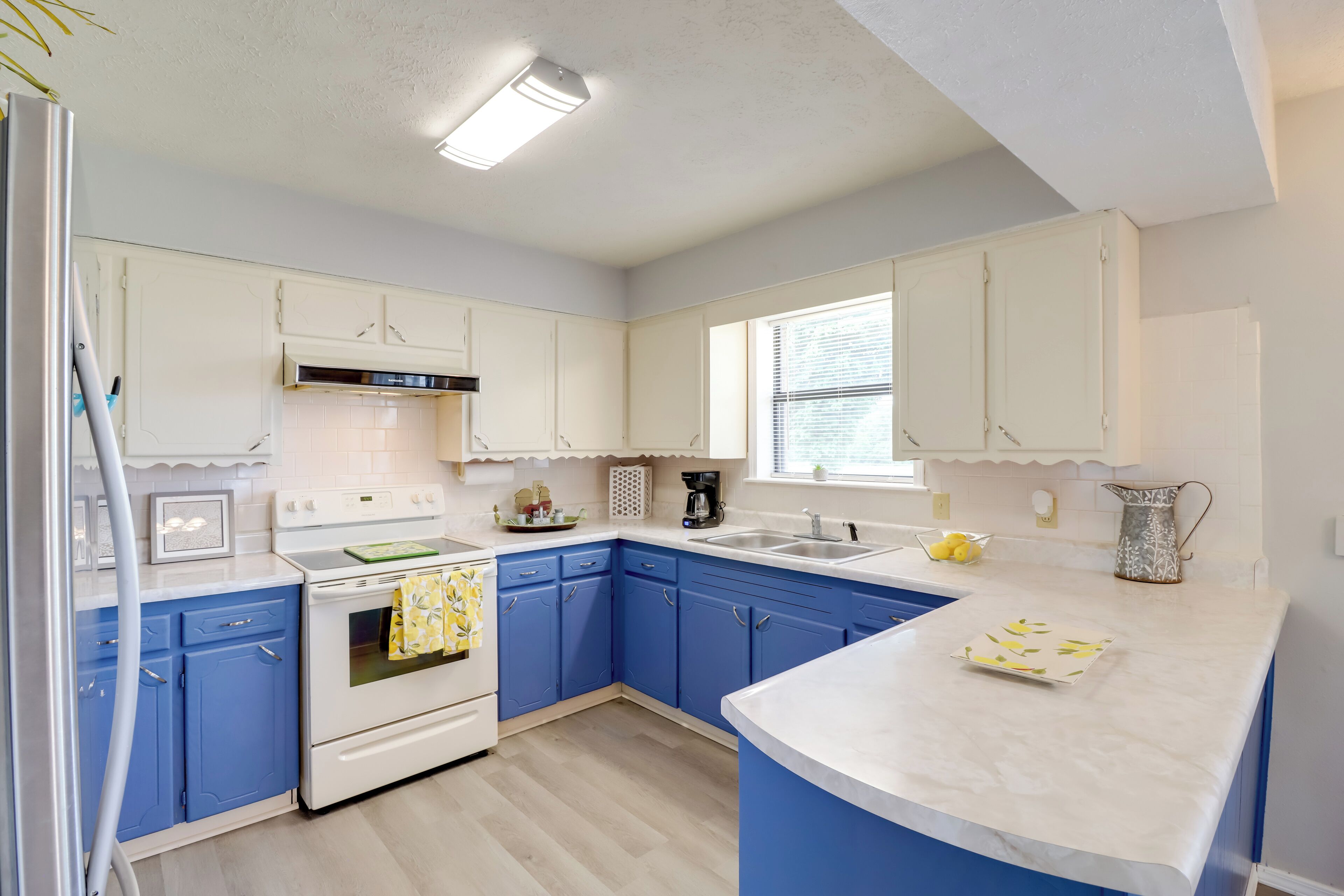 Een moderne keuken met witte en blauwe kastjes, een witte kookplaat en een groot raam.