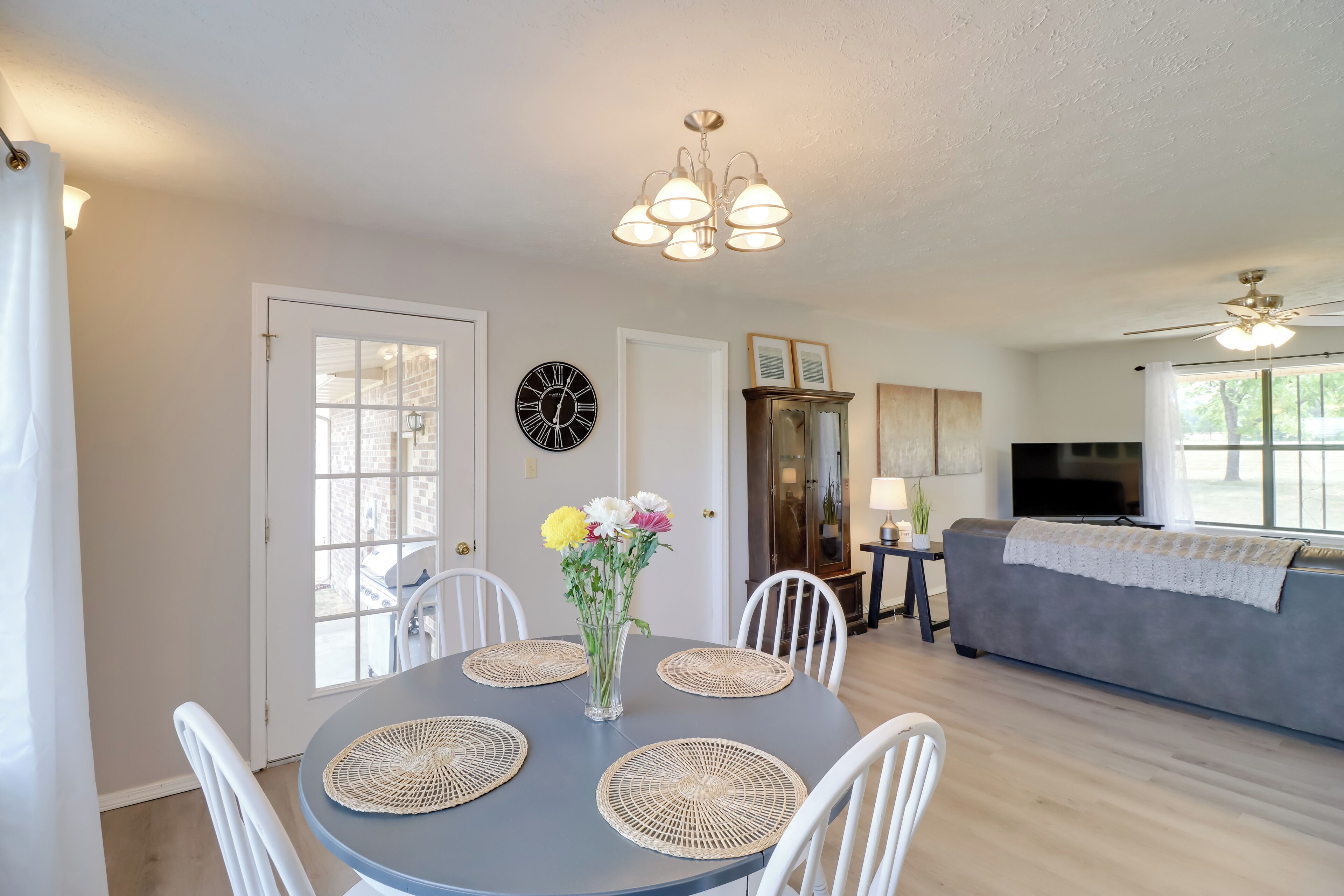 A dining area with a round table, white chairs, a vase with flowers, and a ceiling fan.