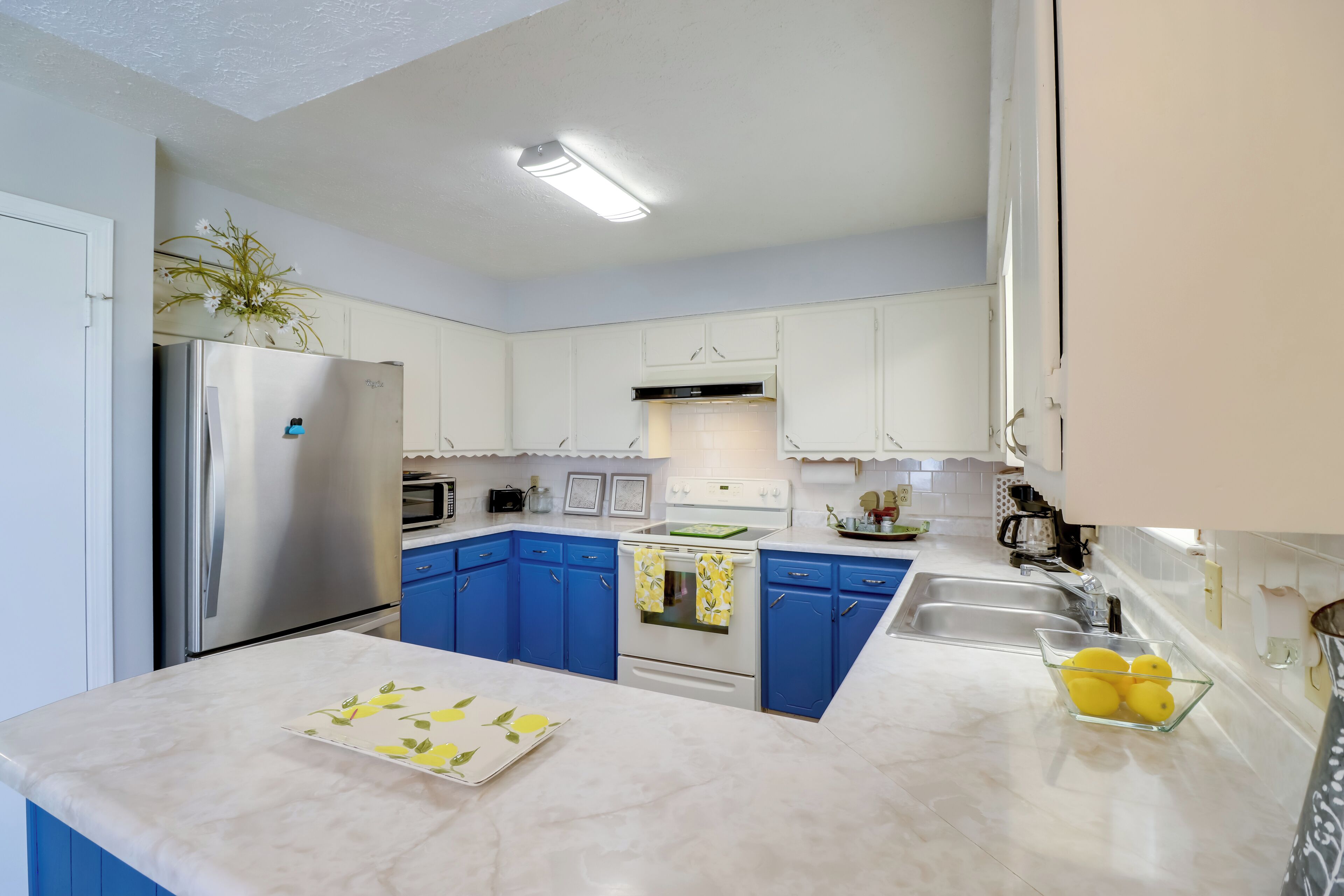 Une cuisine moderne avec des meubles blancs, des touches de bleu, des appareils en acier inoxydable et un plan de travail en marbre.