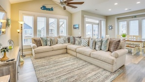 A spacious living room with a beige sectional sofa, a large area rug, and a ceiling fan. - Surf City Home w/ Outdoor Shower: Walk to Beach! (Holly Ridge)