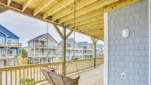 A wooden deck with a hanging chair, a railing, and a view of multi-story buildings in the background. - Surf City Home w/ Outdoor Shower: Walk to Beach! (Holly Ridge)