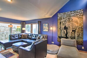 A living room with a sectional sofa, a small ottoman, and a large painting of elephants on the wall. - Puget Sound Home w/ Beautiful Yard & Deck! (Des Moines)