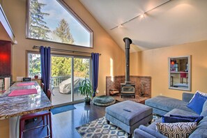 A modern living room with a fireplace, a dining area with a marble countertop, and a large sliding glass door leading to a balcony. - Puget Sound Home w/ Beautiful Yard & Deck! (Des Moines)