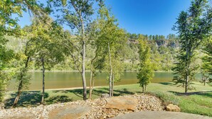 A wooden deck with a stone pathway leading to a lake surrounded by trees. - 'troutfest' Riverfront Norfork Home, Great Fishing (Norfork)