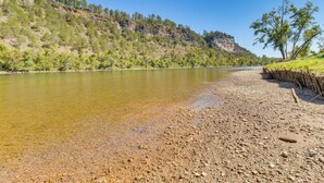 A riverbank with clear water, a rocky shore, and a forested hillside. - 'troutfest' Riverfront Norfork Home, Great Fishing (Norfork)