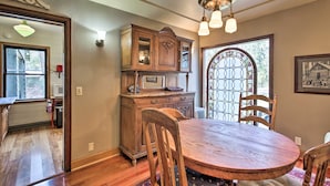 A dining area with a wooden table, chairs, a chandelier, and a stained glass door. - Remote Escape: Riverside Home w/ Scenic Views (Idanha)