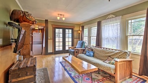 A cozy living room with a sofa, a wooden bench, a decorative trunk, and a large window with curtains. - Remote Escape: Riverside Home w/ Scenic Views (Idanha)