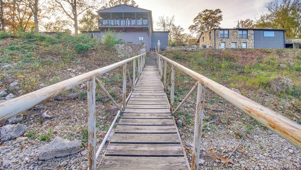 A wooden pathway leading to a building with a balcony, surrounded by trees and vegetation.