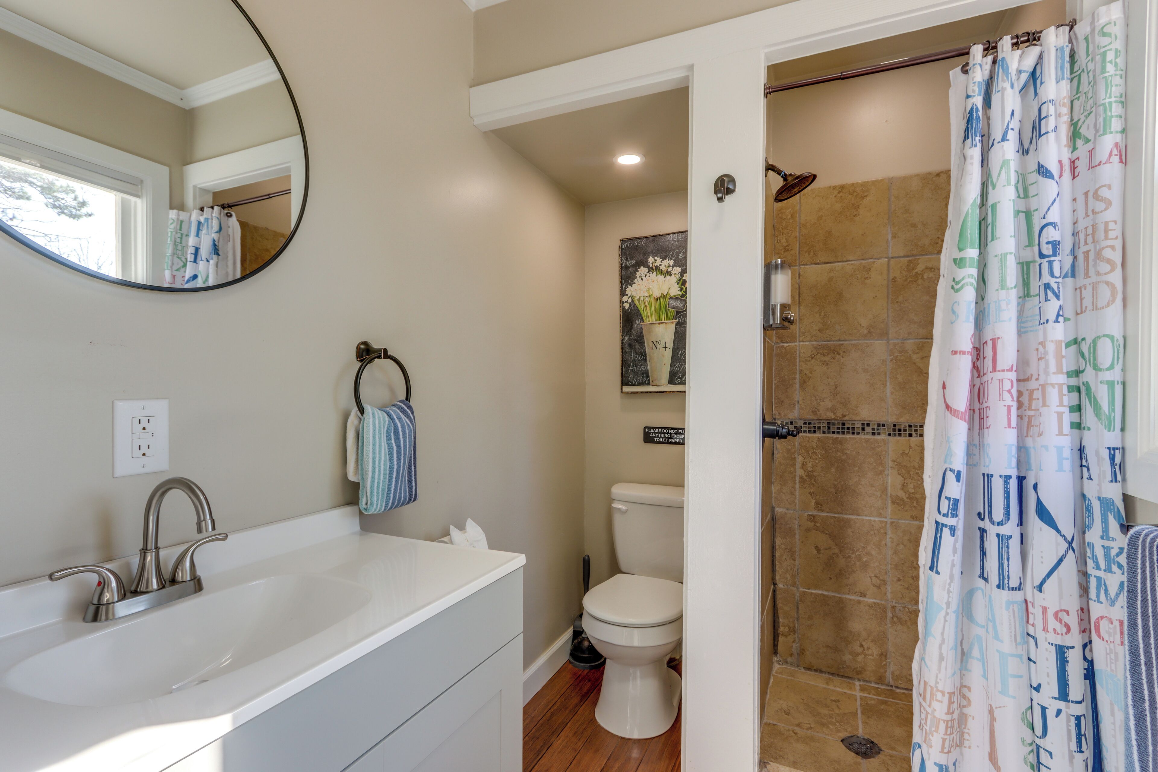 A bathroom with a white sink, a mirror, a toilet, and a shower curtain with text.