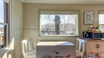 Una habitación con ventana, dos sillas blancas, una mesa, un mueble con electrodomésticos de cocina y un cartel en la pared.