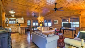 A cozy cabin interior with wooden walls, a kitchen area, a living room with a sofa and a television, and a ceiling fan. - Quaint Bryson City Cottage w/ Smoky Mountain Views (Bryson City)