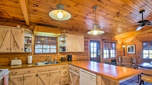 A wooden cabin interior with a kitchen, dining area, and a ceiling fan. - Quaint Bryson City Cottage w/ Smoky Mountain Views (Bryson City)