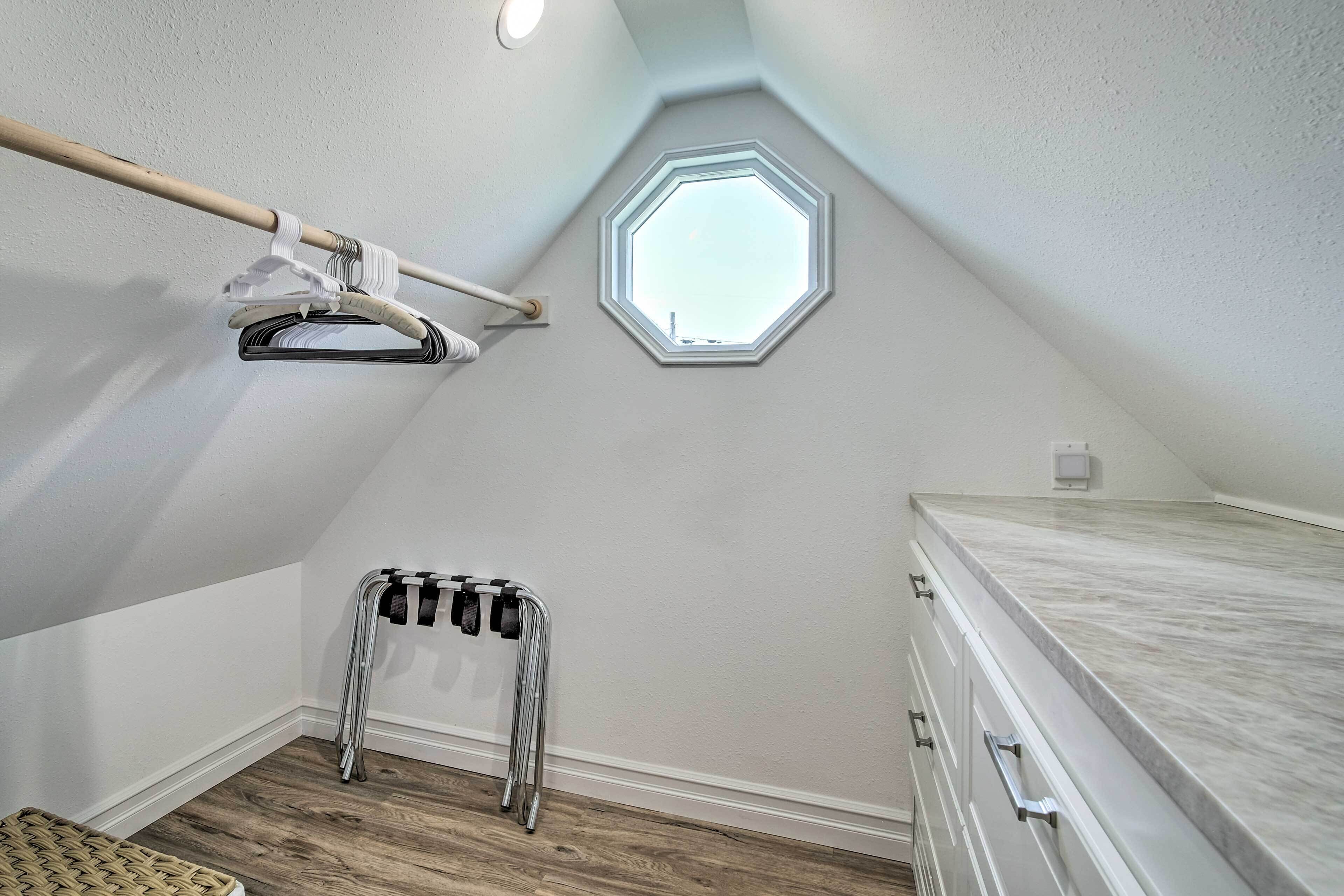 A small, well-lit attic bedroom with a sloped ceiling, a skylight, a wooden floor, a metal drying rack, and a white dresser.