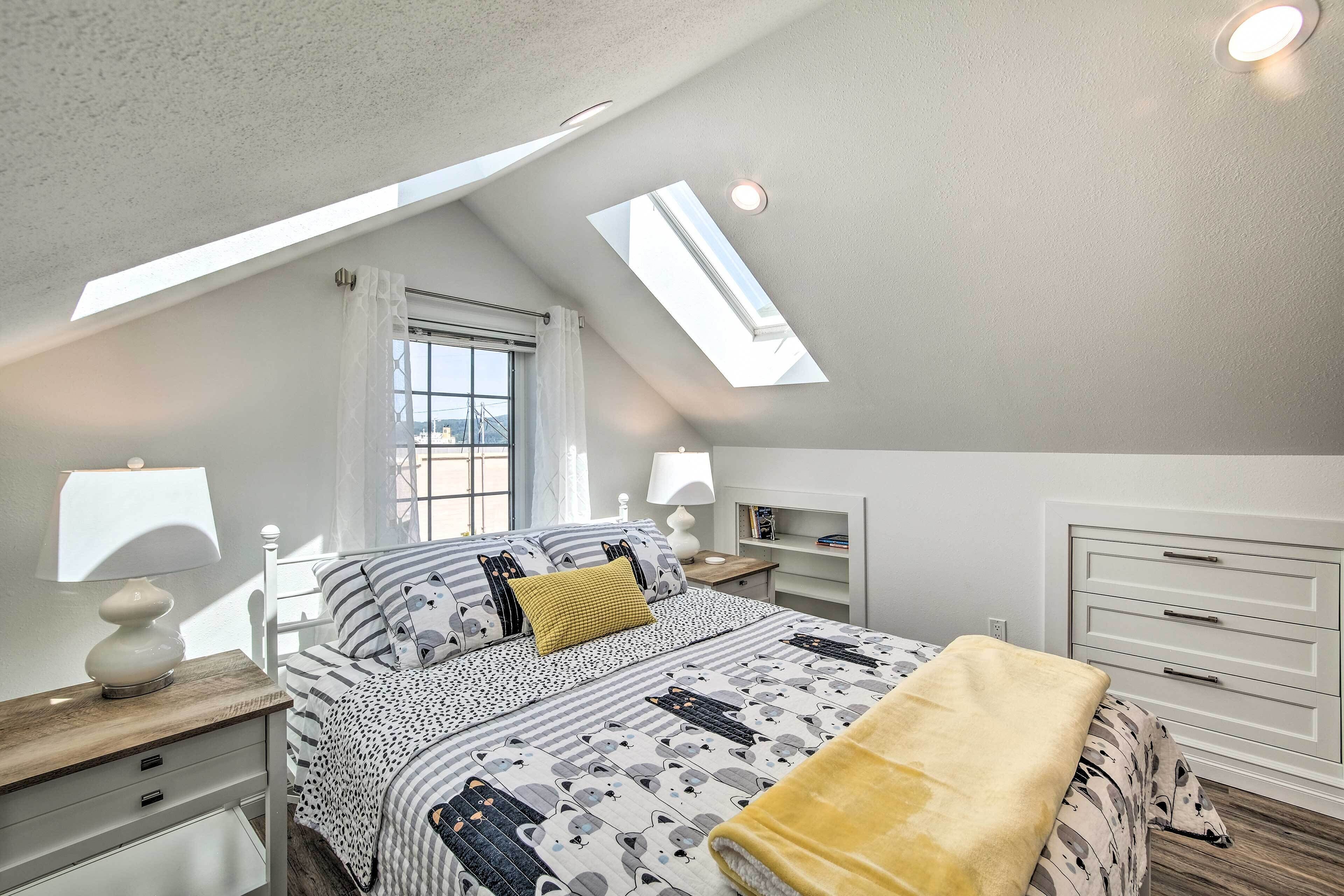 A bedroom with a skylight, a bed with patterned bedding, bedside tables with lamps, and a white dresser.
