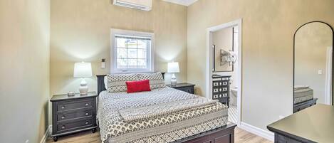A bedroom with a bed, two bedside tables with lamps, a dresser, a mirror, and a window with blinds.