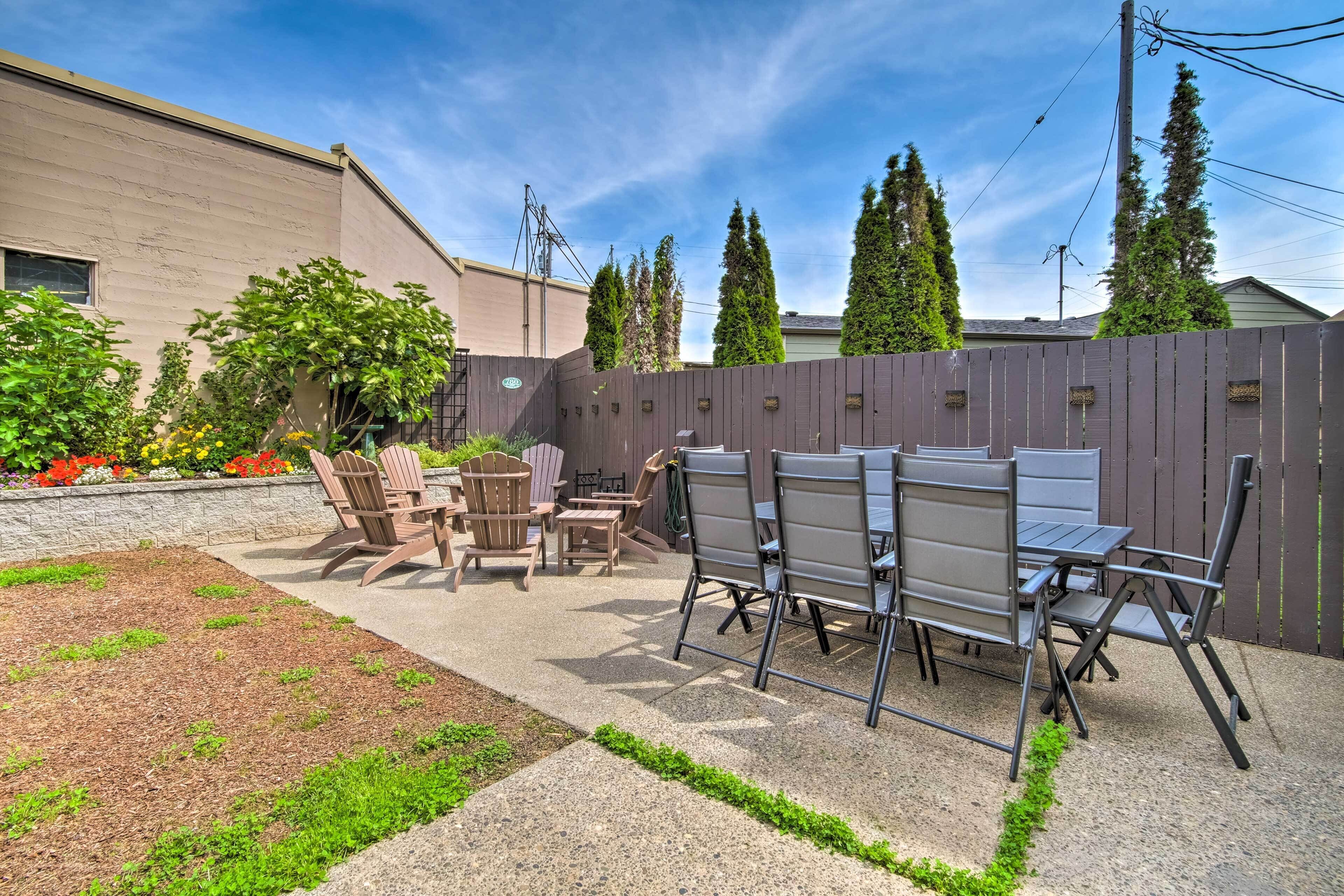 An outdoor patio with a table and chairs, surrounded by a wooden fence and greenery.