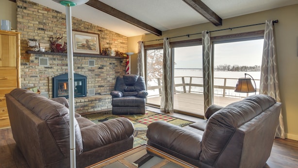 A cozy living room with a fireplace, leather sofas, and a large window overlooking a deck. - Breezy Point House w/ Dock on Pelican Lake! (Pequot Lakes)