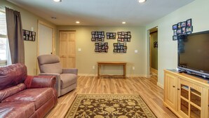 A living room with a leather couch, a beige armchair, a wooden coffee table, a TV on a wooden stand, and a wall decorated with framed photos. - Breezy Point House w/ Dock on Pelican Lake! (Pequot Lakes)