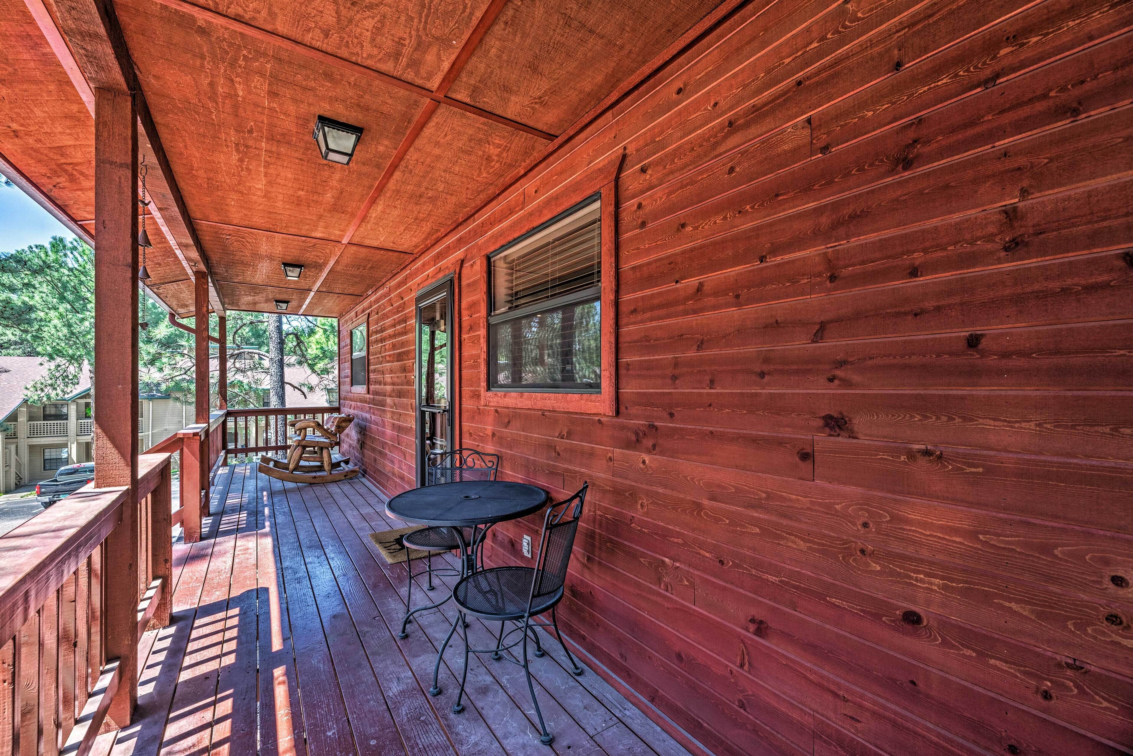 A wooden porch with a table and chairs, a rocking chair, and a view of the surrounding area.