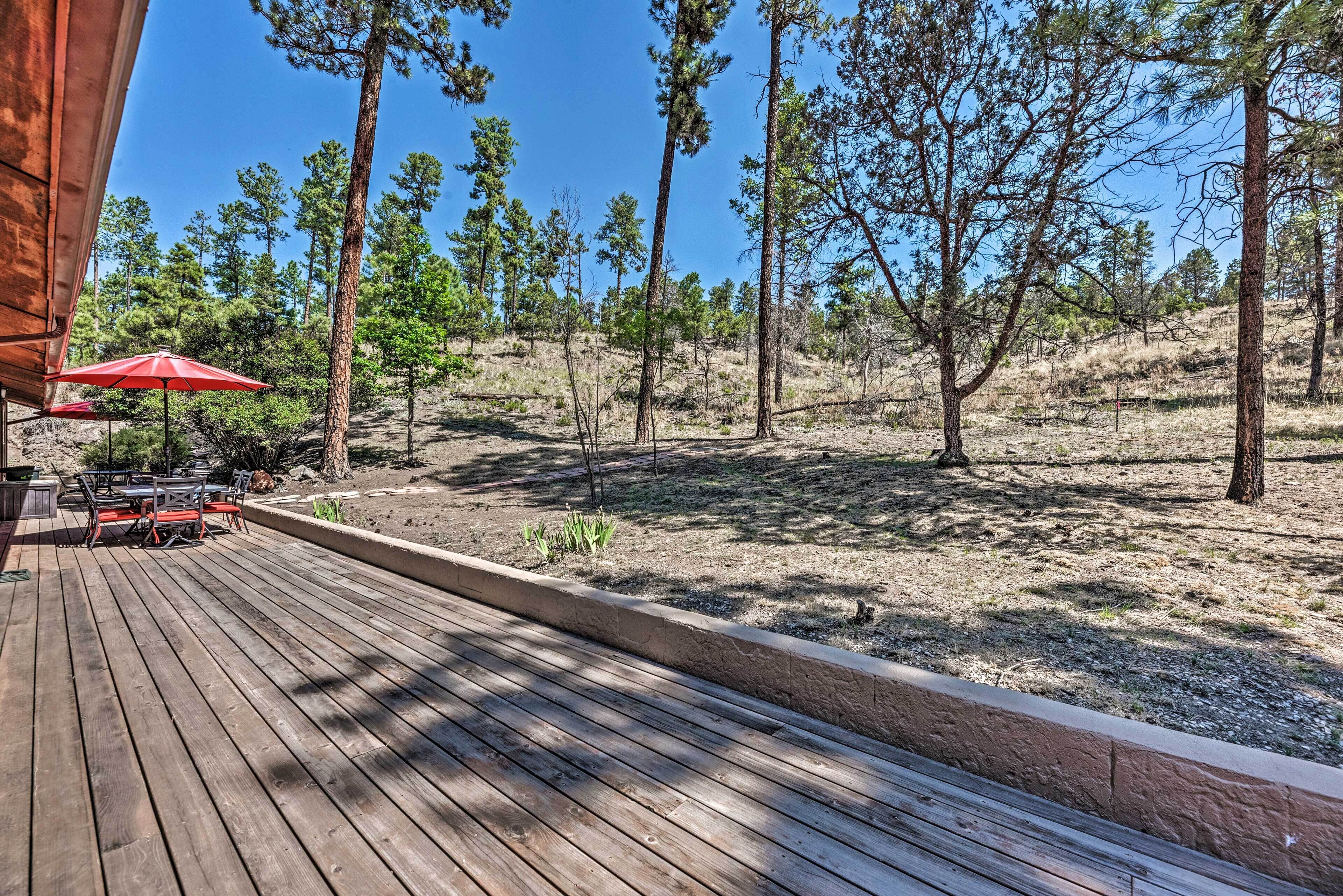 A wooden deck with a table and chairs, surrounded by a landscaped area with trees and a clear sky.