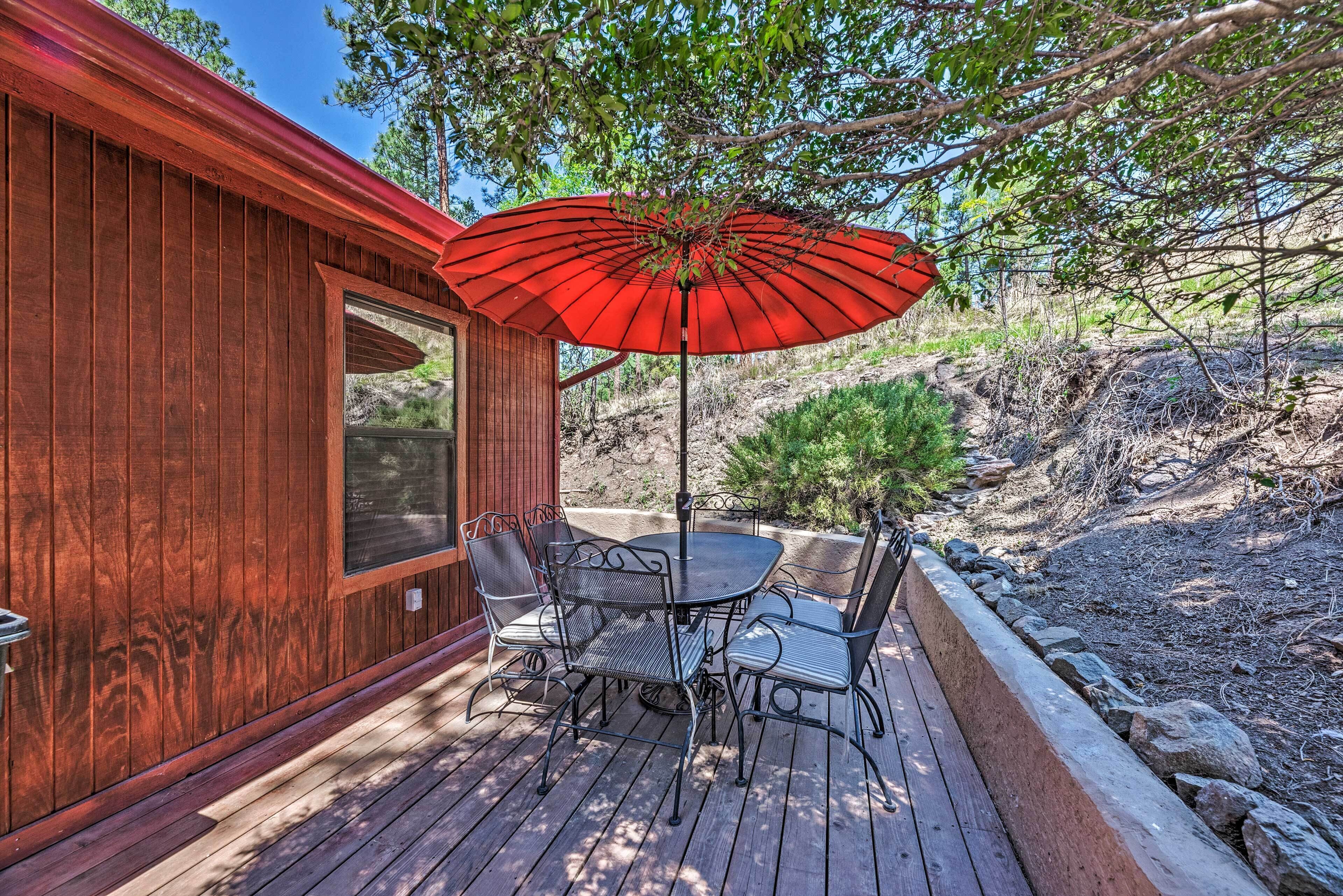 A wooden deck with a table and chairs, a red umbrella, and a view of a natural landscape.