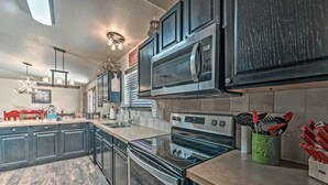 A modern kitchen with dark cabinetry, stainless steel appliances, and a wooden floor. - Wooded Ruidoso Hideaway w/ Deck: Ski, Hike & Golf! (Ruidoso)