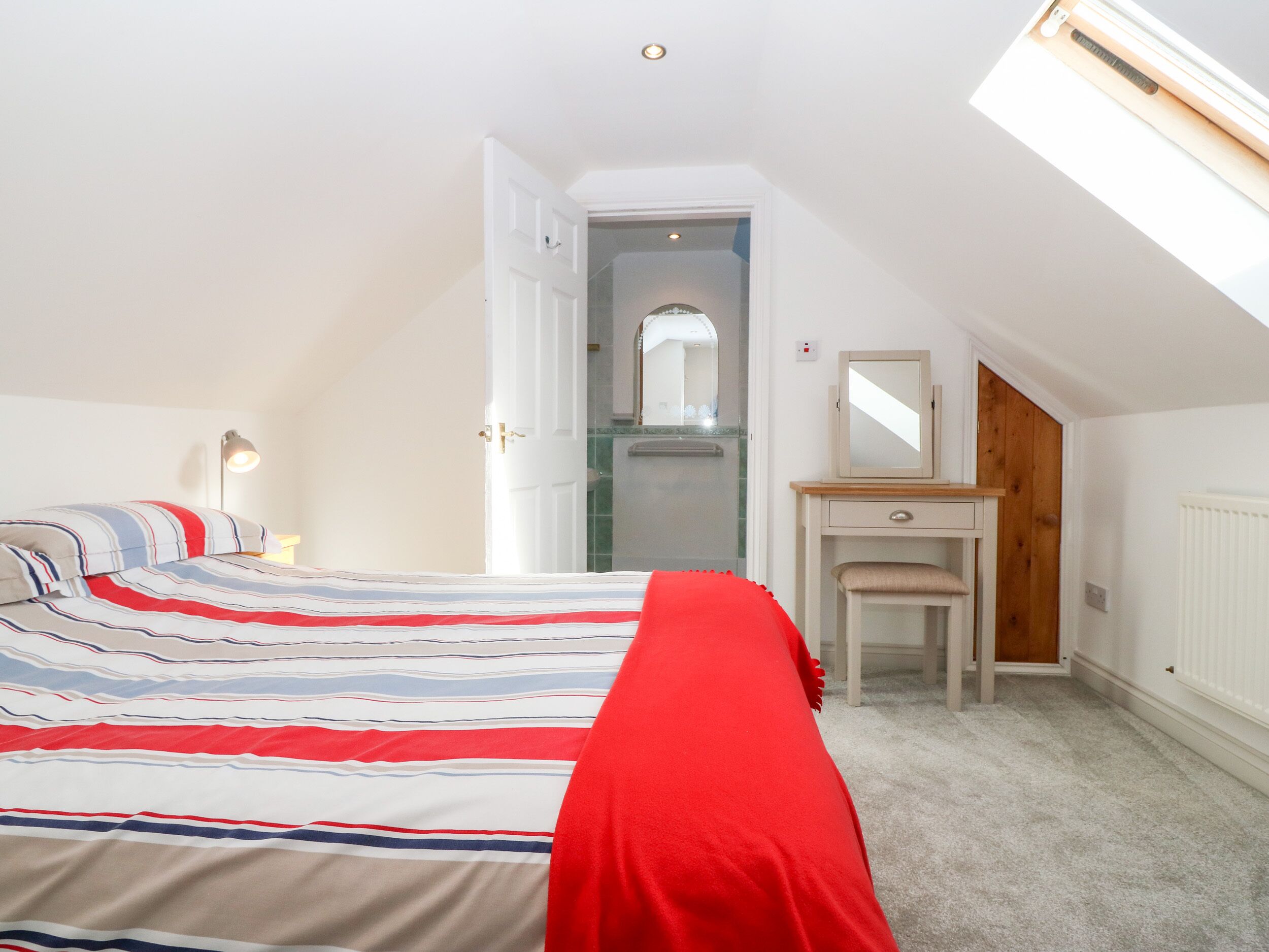 A bedroom with a bed, a dresser, a mirror, and a skylight.