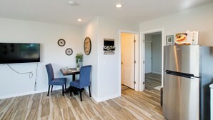 A modern kitchen with a large refrigerator, a dining area with two chairs, a flat-screen TV, and a small table. - Peaceful Peoria Bungalow w/ Grill & Pool! (Peoria)