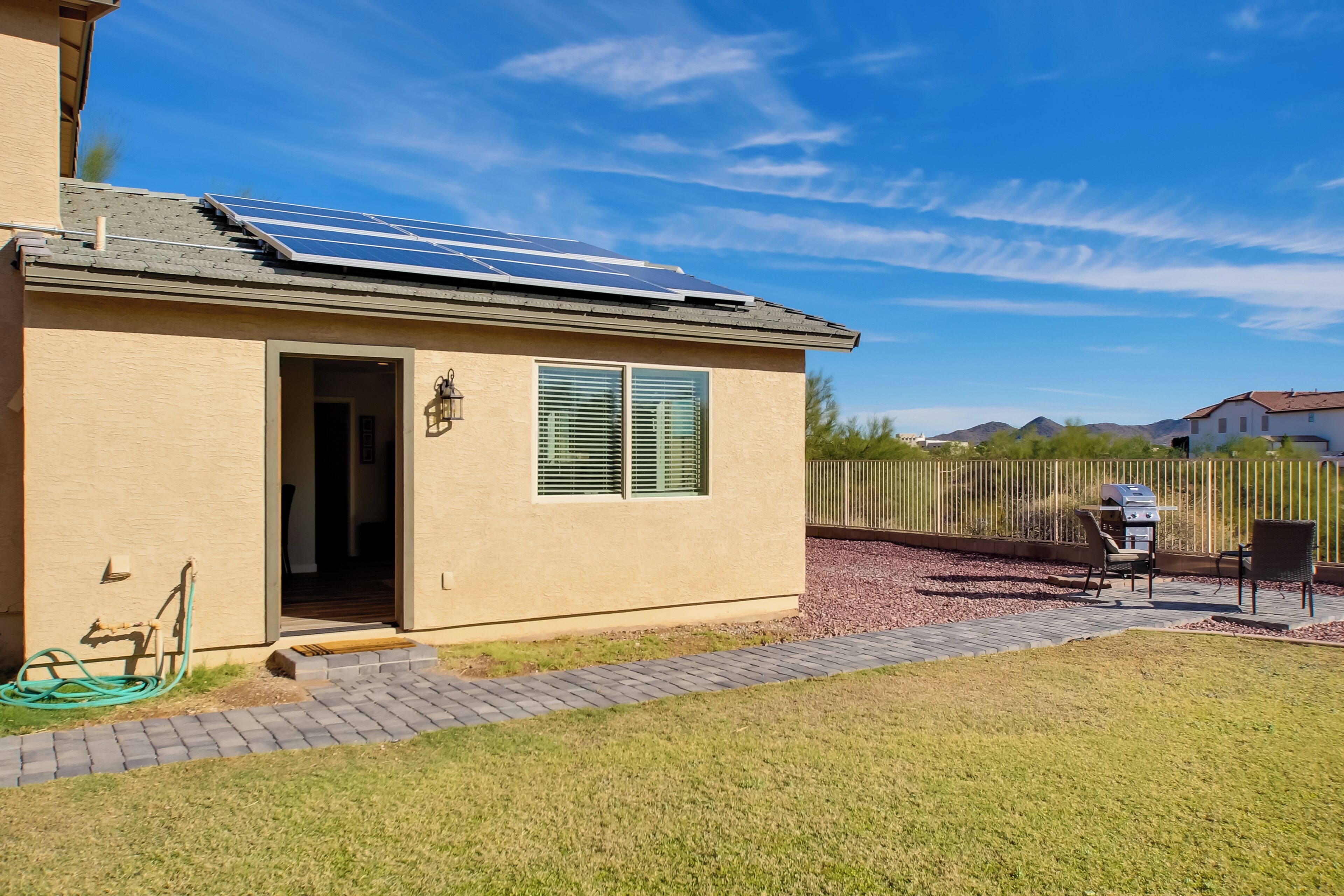 A house with solar panels on the roof, a paved driveway, and a fenced backyard with outdoor furniture.