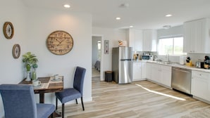 A modern kitchen with white cabinets, a stainless steel refrigerator, and a dining area with a wooden table and chairs. - Peaceful Peoria Bungalow w/ Grill & Pool! (Peoria)