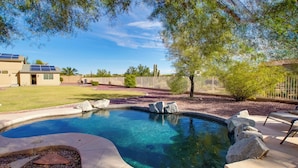 A swimming pool with a curved design, surrounded by a stone deck and a wooden fence. - Peaceful Peoria Bungalow w/ Grill & Pool! (Peoria)