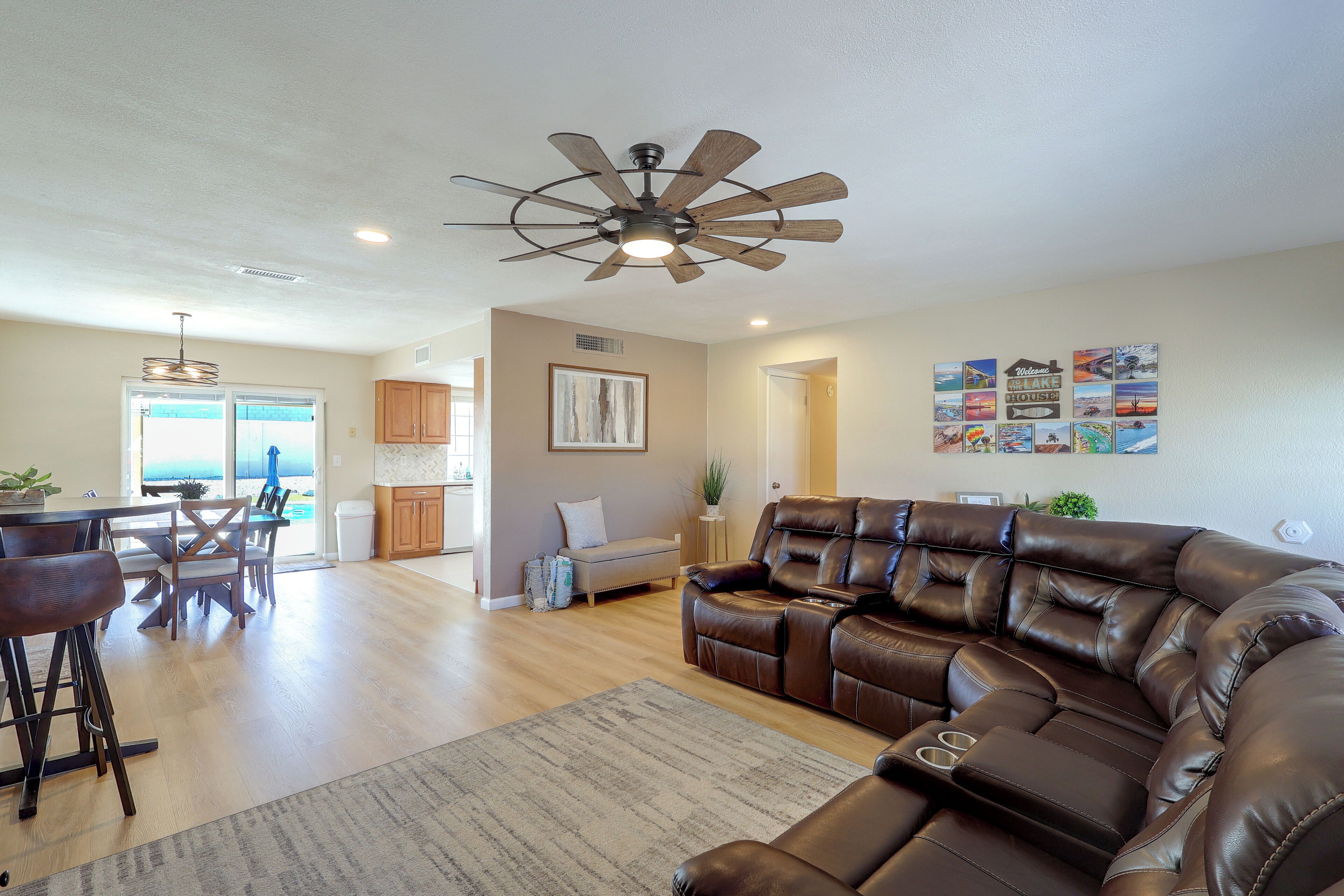 A spacious living room with a leather sectional sofa, a dining area with a table and chairs, a kitchen with wooden cabinets, and a ceiling fan.