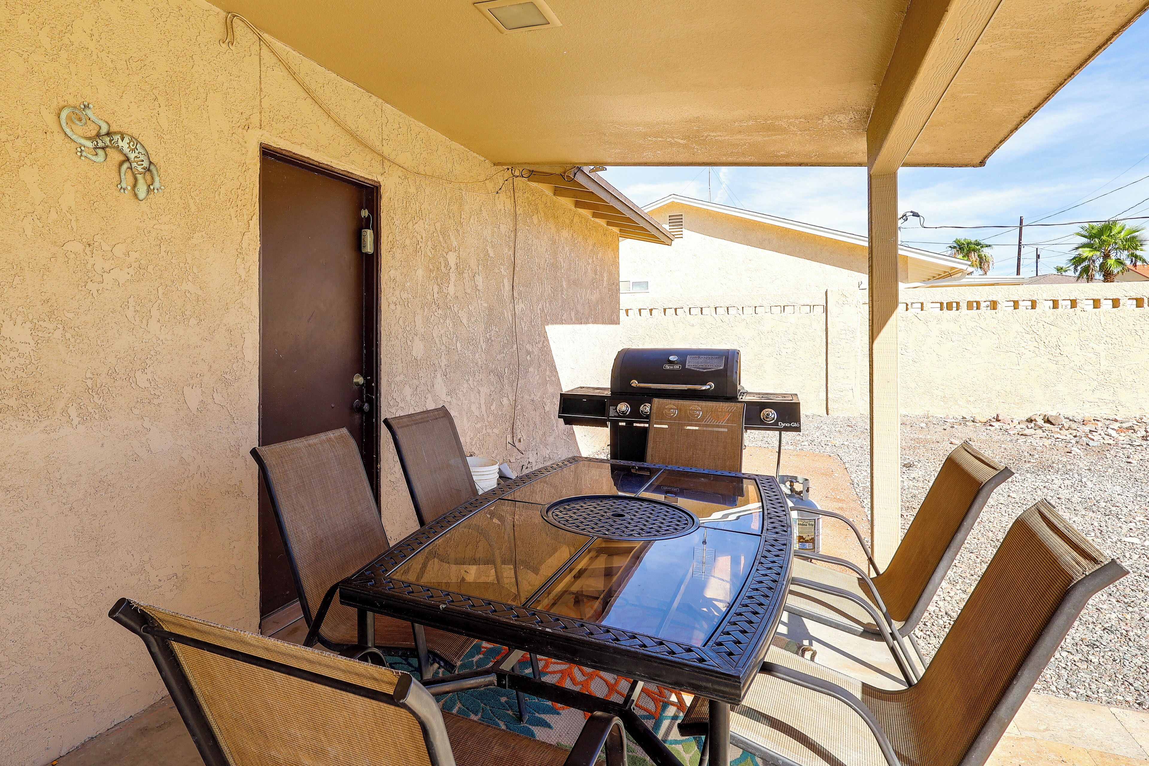Eine Terrasse im Freien mit einem Glastisch, Metallstühlen und einem Grill.