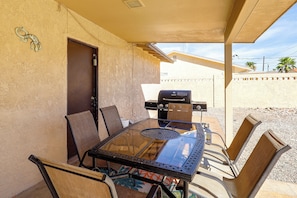Eine Terrasse im Freien mit einem Glastisch, Metallstühlen und einem Grill.