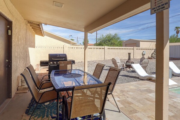 An outdoor patio with a grill, dining table, chairs, and a pool area.