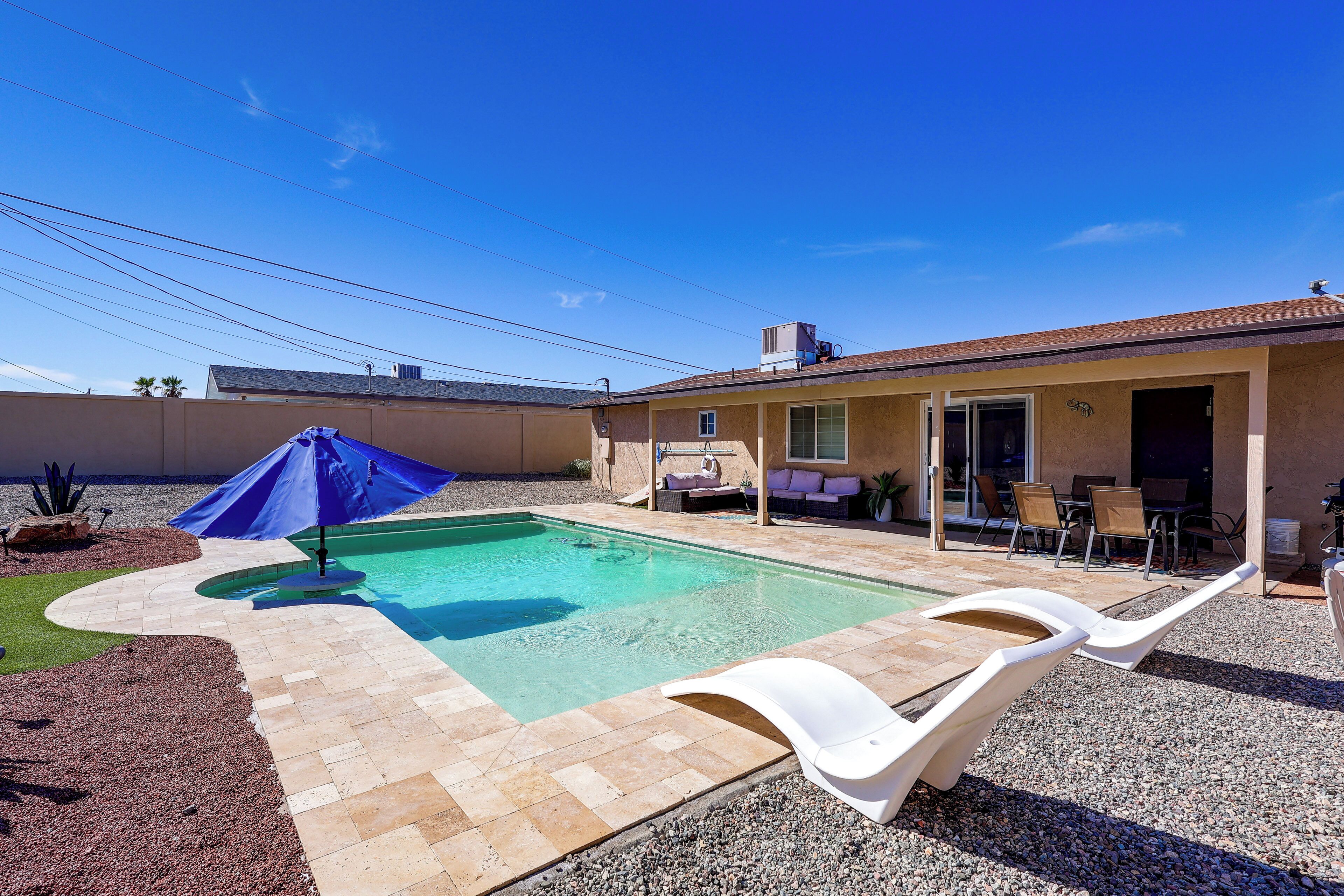 A backyard with a swimming pool, patio furniture, and a covered seating area.