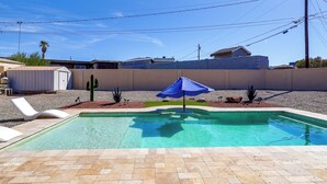 A swimming pool with a blue umbrella, surrounded by a pebble border, and a white lounge chair. - 5 Mi to Lake Havasu: Home w/ Yard & Pool (Lake Havasu City)