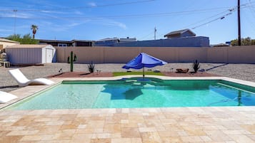 Une piscine avec un parasol bleu, bordée de galets, et une chaise longue blanche.