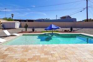 A swimming pool with a blue umbrella, surrounded by a pebble border, and a white lounge chair.