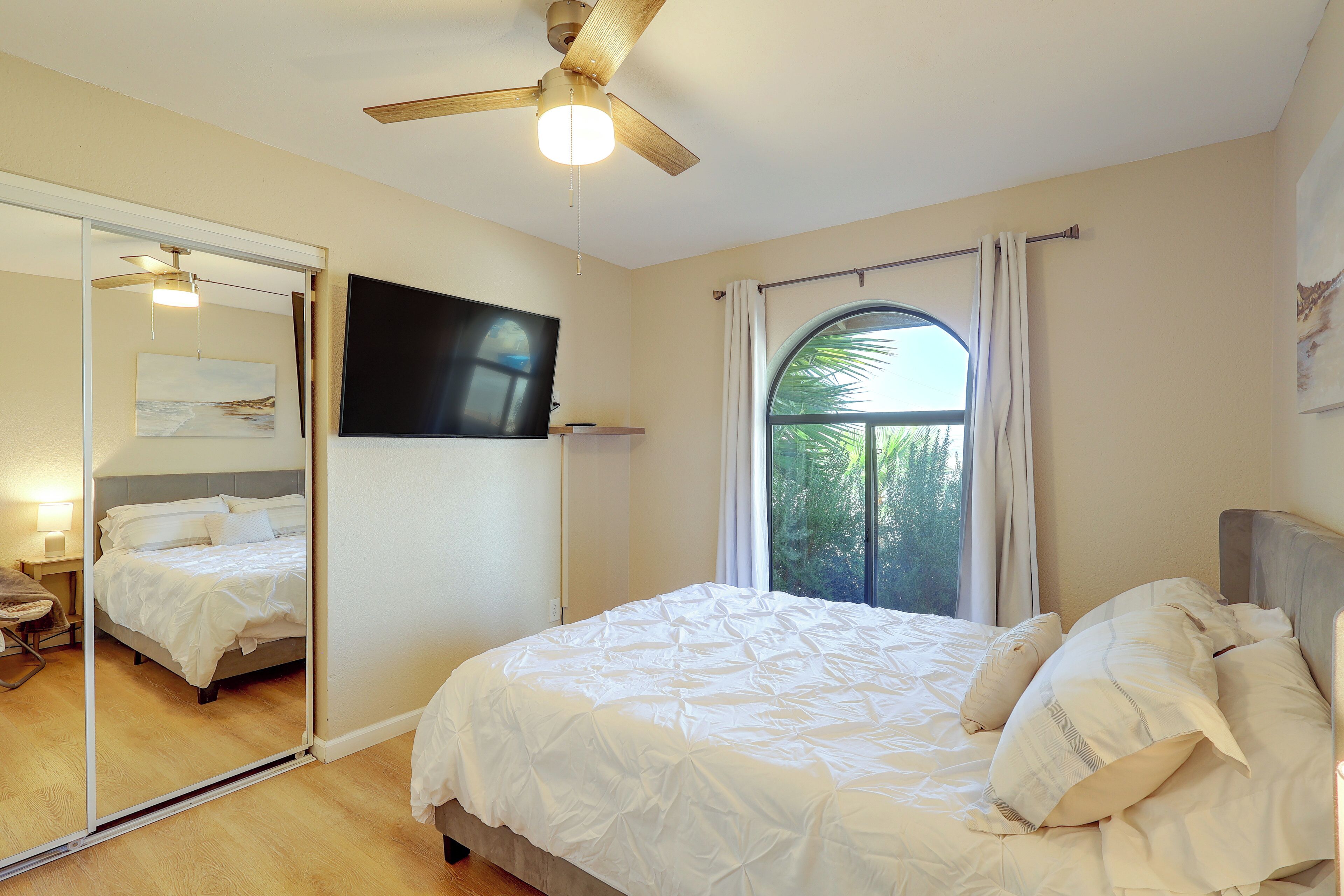 Une chambre à coucher avec un lit, un ventilateur de plafond, un grand miroir et une fenêtre.