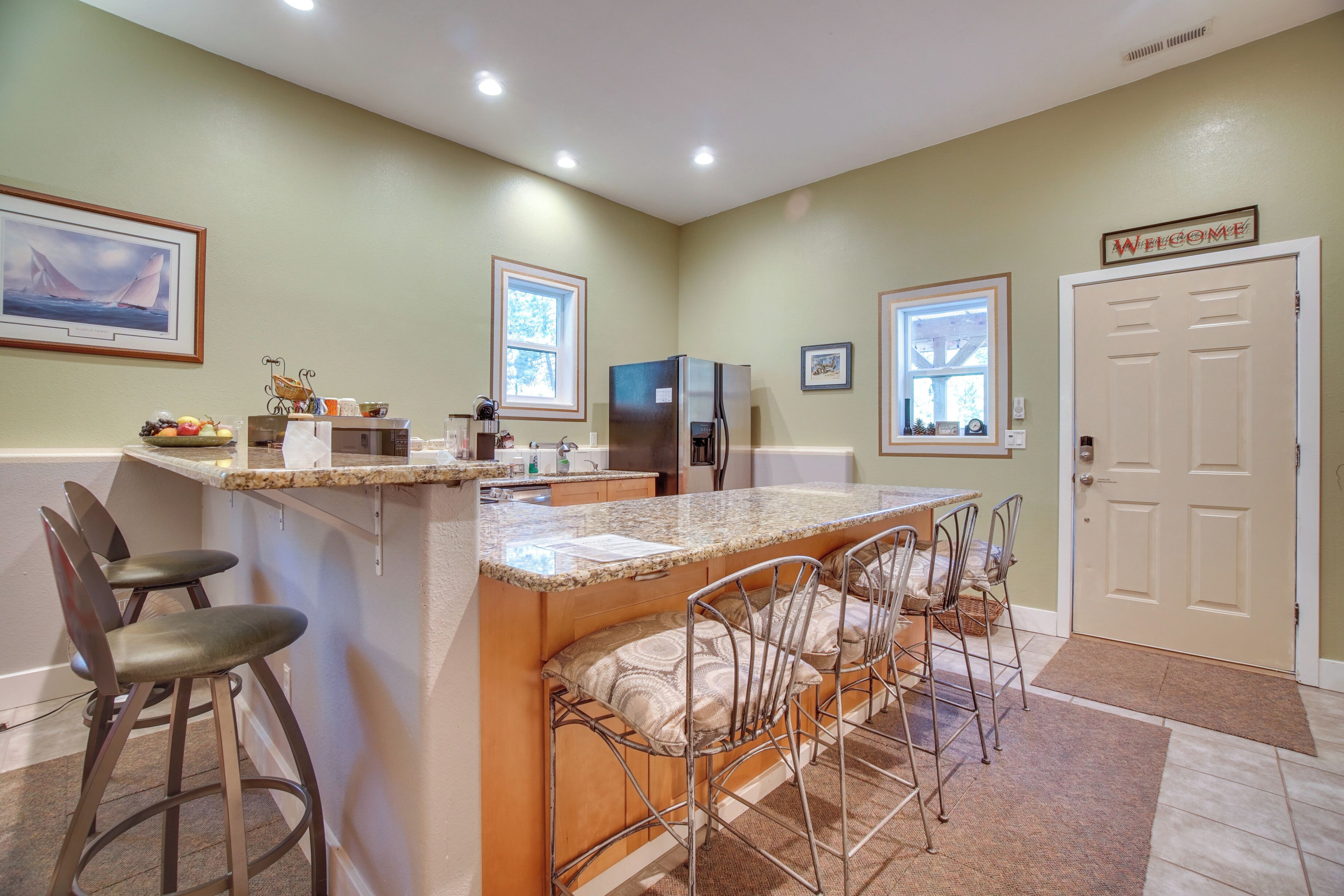 A kitchen with a central island, bar stools, a refrigerator, and a microwave.