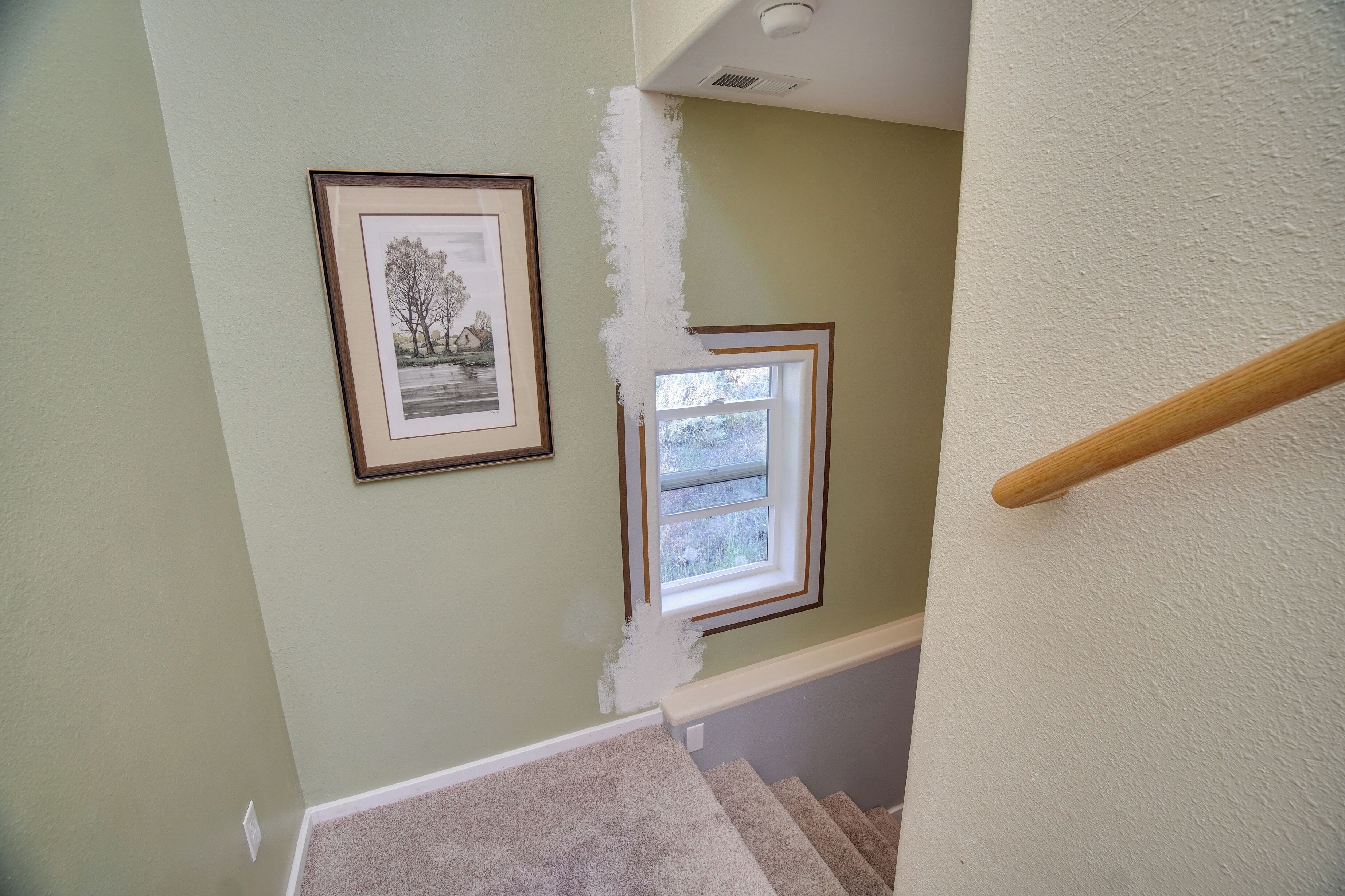 A staircase with a carpeted landing, a framed picture on the wall, and a window with a view of trees.