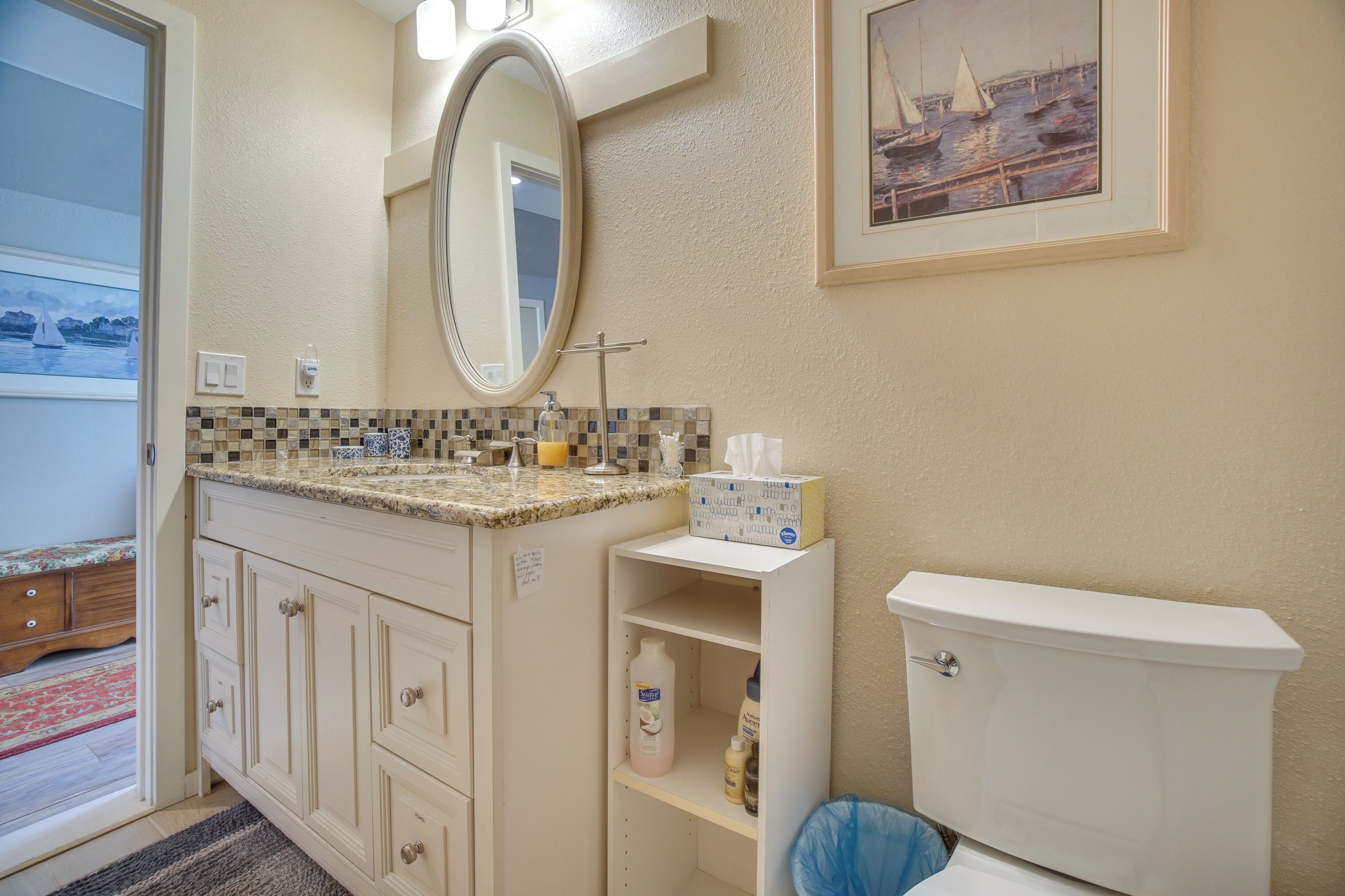 Un bagno con il water, un lavabo e uno specchio. C'è un quadro appeso al muro e una finestra con vista su barche.