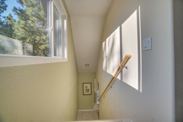 A narrow stairway with a window on the left, a wooden handrail on the right, and a framed picture on the wall.