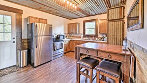 A modern kitchen with wooden cabinets, stainless steel appliances, and a wooden dining table with stools.