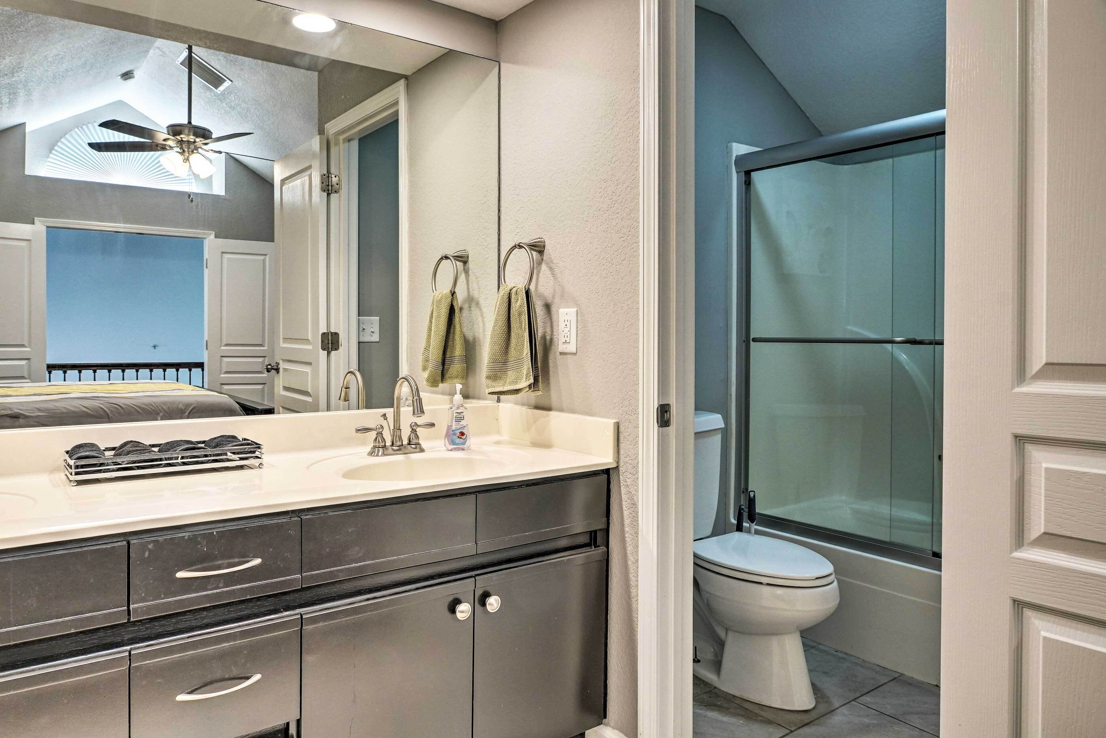 A bathroom with a large mirror, a ceiling fan, a sink with a soap dispenser, and a toilet.
