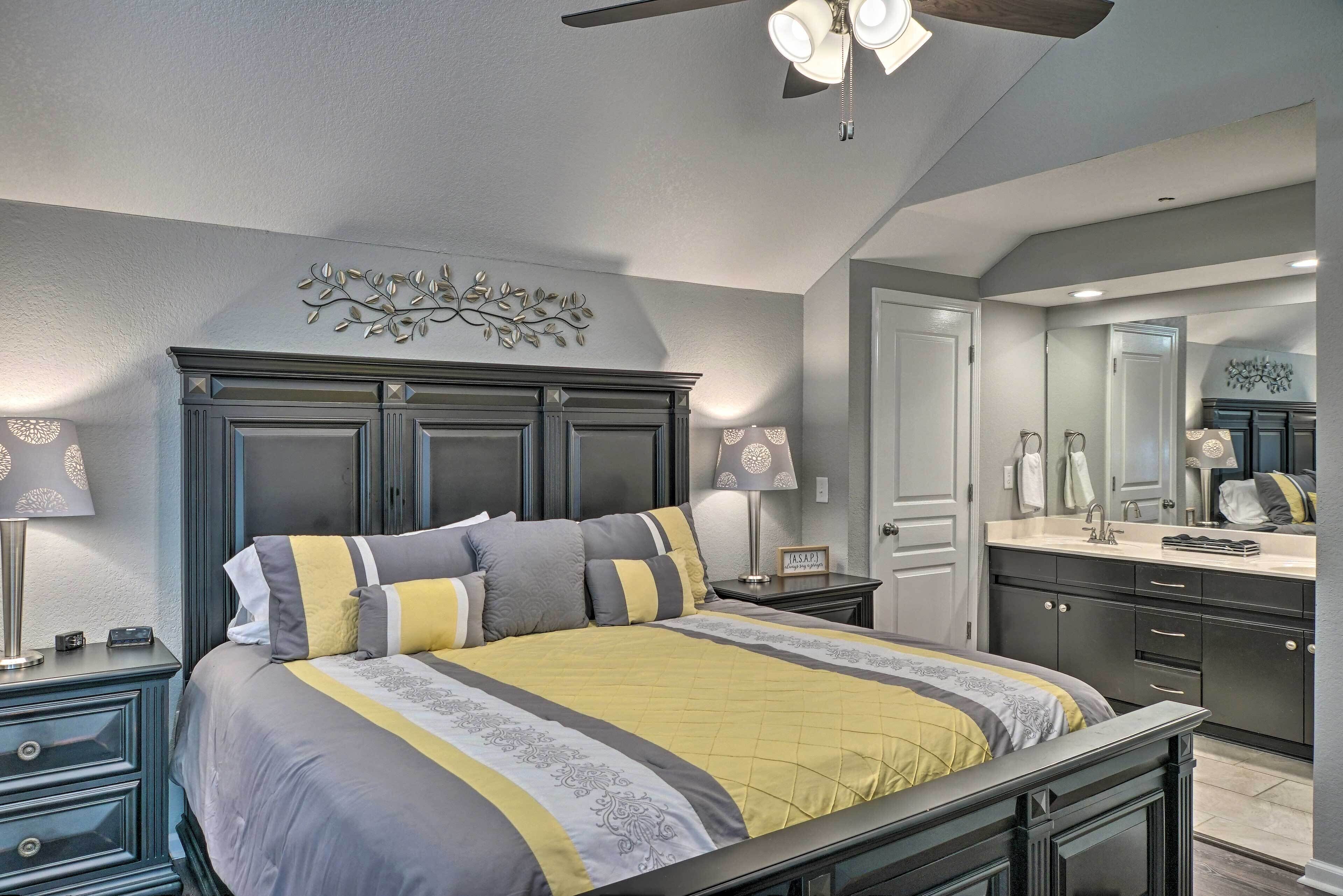 A bedroom with a bed, nightstands, a ceiling fan, and a bathroom with a sink and mirror.