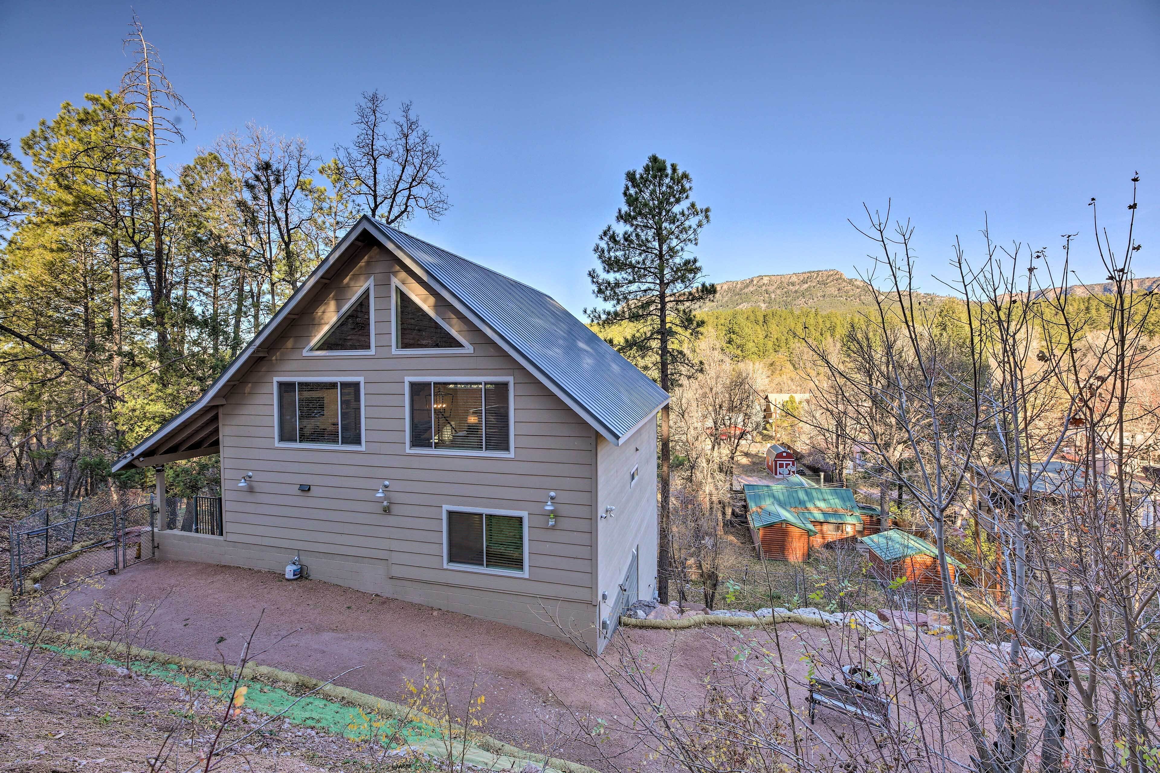 A two-story house with a sloped roof, a fenced yard, and a mountainous backdrop.