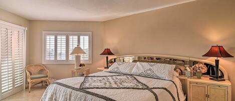 A bedroom with a large bed, two bedside lamps, a nightstand, a chair, and a window with blinds.